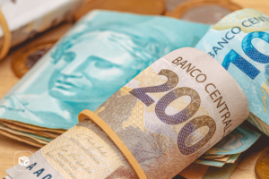 Notas de 200 e 100 reais em close-up, com moedas ao fundo.
