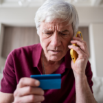 Homem idoso preocupado ao telefone com cartão de crédito azul, possível golpe de RPV